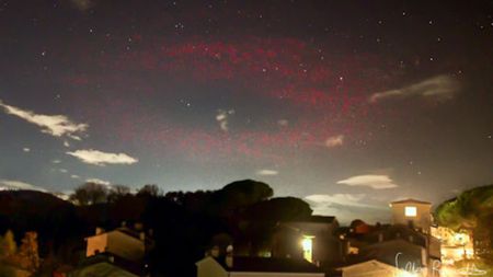 A photograph of a blurry red ring of light in the night sky above a town in Italy