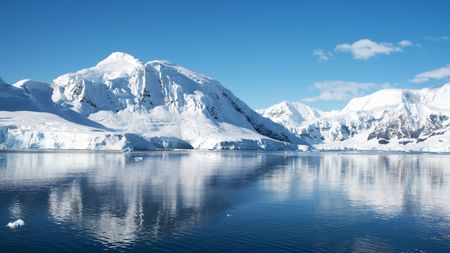 On a rare clear day, snowy mountains are reflected in the placid waters of a tranquil cove in the Antarctic Peninsula.